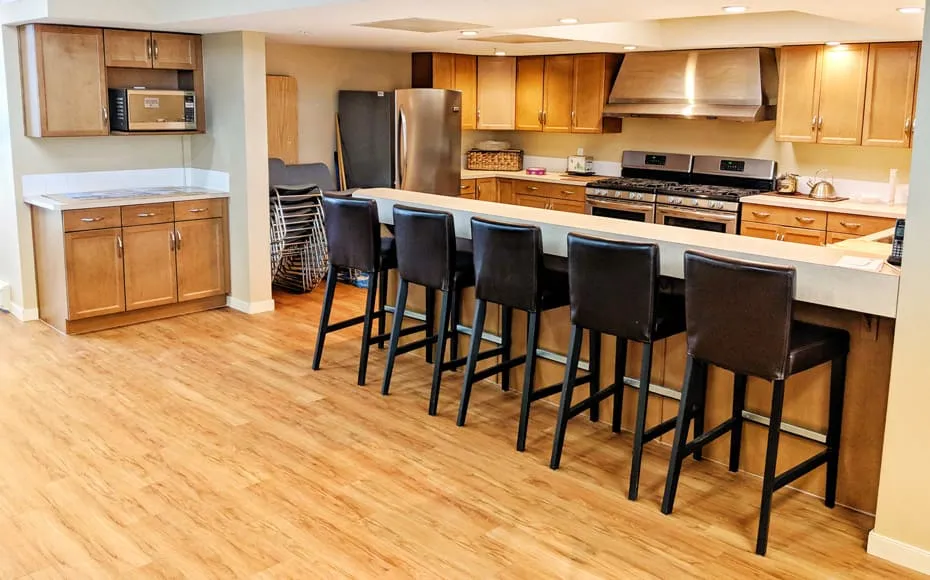 The community kitchen at Inglewood House, with wood cabinets, stainless steel appliances and a long counter with bar stools