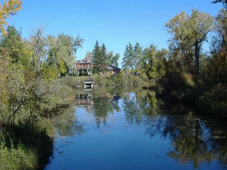 A still pond surrounded by trees and a house, reflecting the sky, in Inglewood